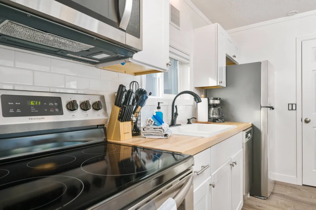 A modern kitchen space with stainless steel appliances, a wooden countertop, a sink area, and a handy knife block. The layout is open and functional, with natural light illuminating the polished surfaces, inviting culinary creativity.