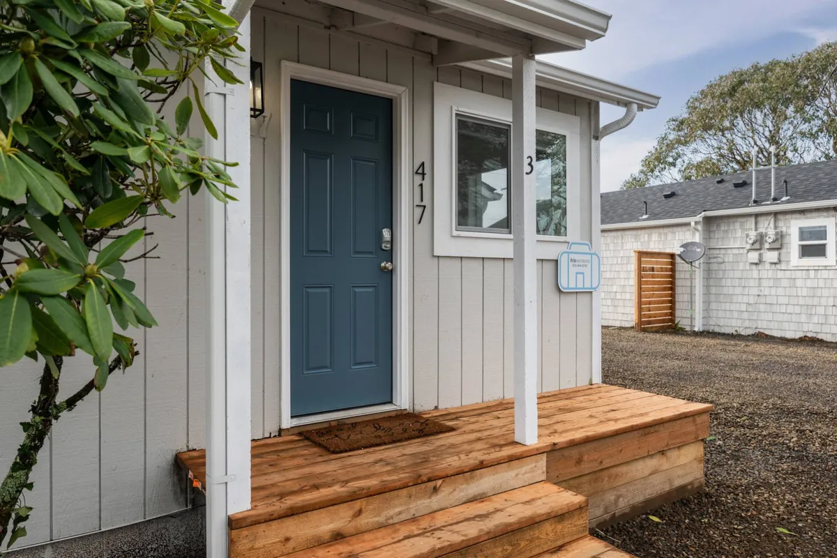 The exterior view features a charming blue front door, wooden steps, and house numbers, creating a warm and inviting first impression of the cottage. The porch area hints at the shared outdoor community spaces mentioned in the section.