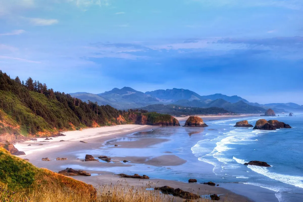 A scenic view of the beach with ocean waves, striking rock formations, and distant mountains, capturing the natural beauty just beyond the cottages.